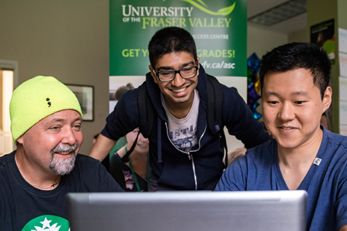 Three students looking at a computer screen inside a classroom